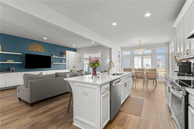 kitchen with a sink, light wood-type flooring, appliances with stainless steel finishes, white cabinetry, and a kitchen island with sink