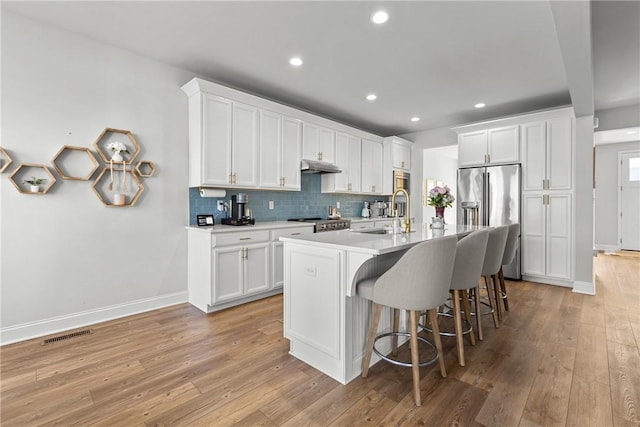 kitchen with a breakfast bar area, a sink, decorative backsplash, stainless steel appliances, and under cabinet range hood