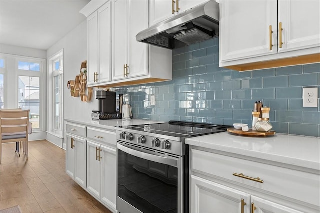 kitchen featuring backsplash, under cabinet range hood, light countertops, stainless steel range with electric stovetop, and light wood-style floors