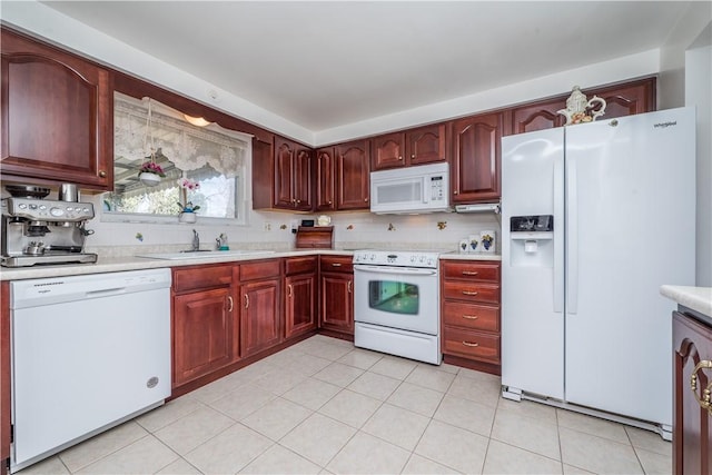 kitchen with a sink, white appliances, reddish brown cabinets, and light countertops