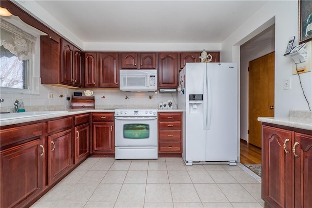 kitchen with tasteful backsplash, light countertops, light tile patterned floors, white appliances, and reddish brown cabinets