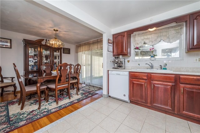 kitchen with a sink, tasteful backsplash, an inviting chandelier, light countertops, and dishwasher