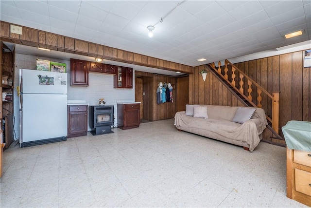 living area with stairway, wooden walls, light floors, and a wood stove