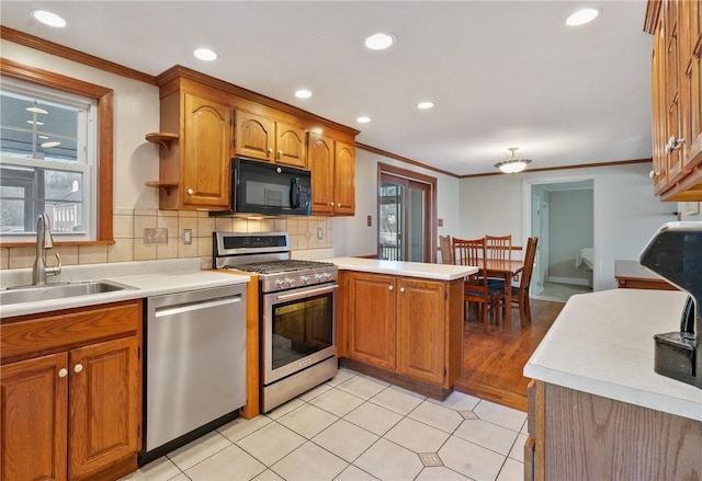 kitchen featuring brown cabinets, appliances with stainless steel finishes, a peninsula, and a sink