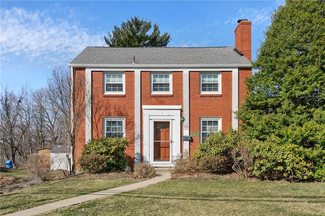 view of front of home featuring a front lawn, brick siding, and a chimney