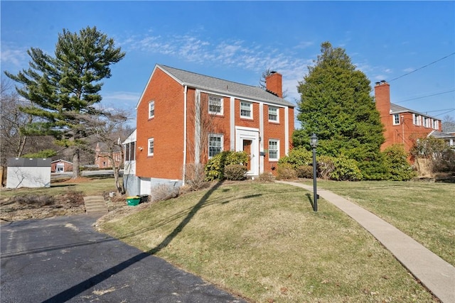 view of front of home featuring a front yard, brick siding, and a chimney