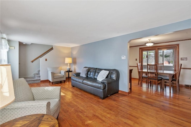 living area featuring arched walkways, stairway, baseboards, and wood finished floors