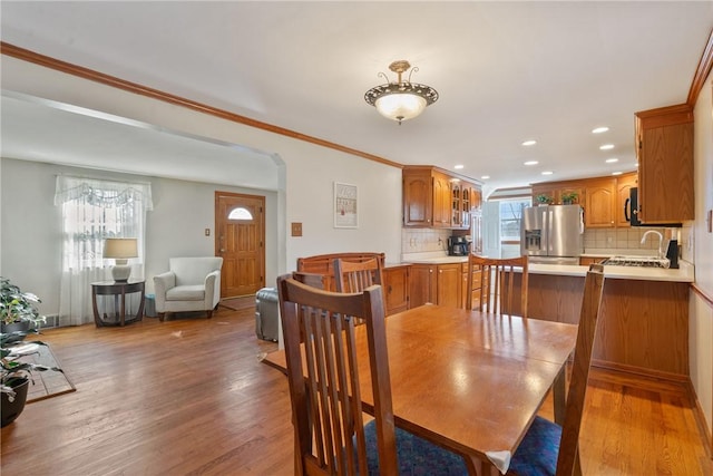 dining area featuring recessed lighting, light wood-type flooring, arched walkways, and crown molding