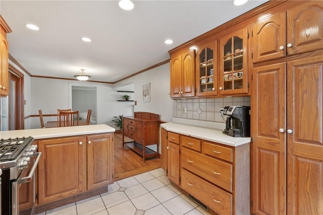 kitchen featuring brown cabinetry, crown molding, glass insert cabinets, and stainless steel stove