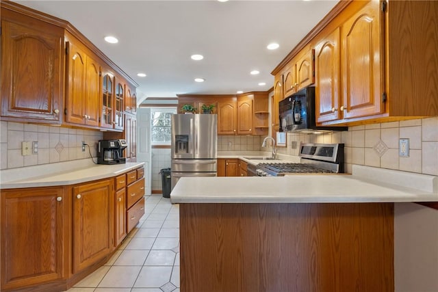 kitchen with a peninsula, light tile patterned flooring, a sink, appliances with stainless steel finishes, and brown cabinets