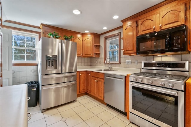 kitchen featuring brown cabinets, ornamental molding, a sink, stainless steel appliances, and light countertops