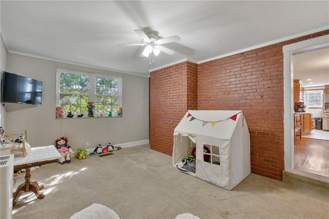 recreation room featuring a ceiling fan, brick wall, carpet flooring, and ornamental molding