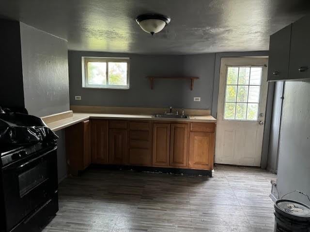 kitchen featuring black range with gas stovetop, a sink, light countertops, refrigerator, and open shelves