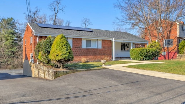 view of front of property with solar panels, a front lawn, brick siding, and roof with shingles