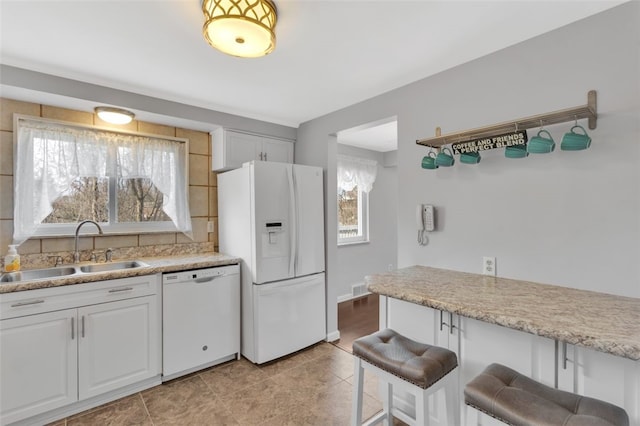 kitchen with white appliances, visible vents, a sink, a kitchen bar, and backsplash