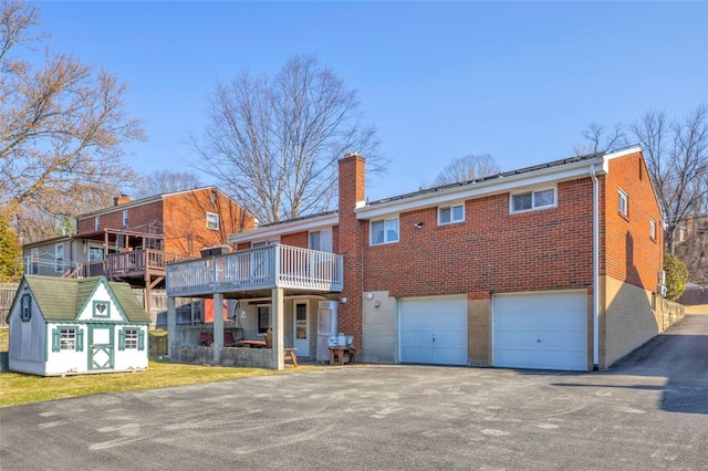 back of property with an attached garage, a chimney, aphalt driveway, a lawn, and brick siding