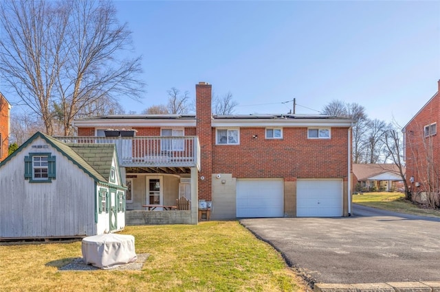 rear view of property featuring brick siding, aphalt driveway, a chimney, a yard, and a garage