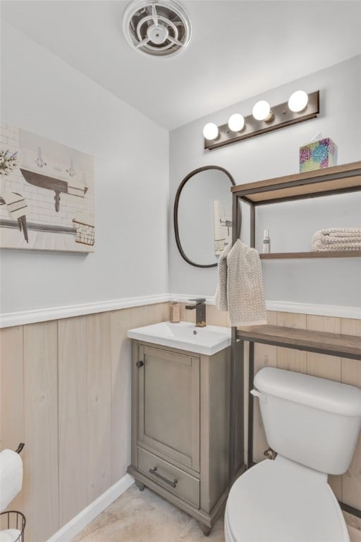 half bath with visible vents, toilet, a wainscoted wall, and vanity