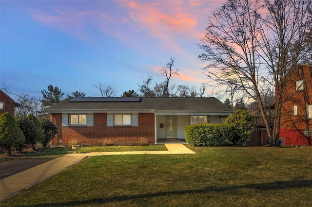 single story home featuring brick siding, solar panels, and a front lawn