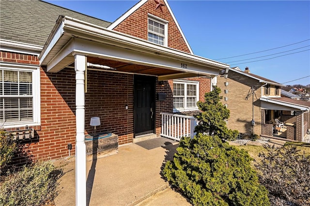 property entrance featuring brick siding and a shingled roof