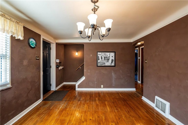 unfurnished dining area featuring visible vents, an inviting chandelier, baseboards, and hardwood / wood-style flooring