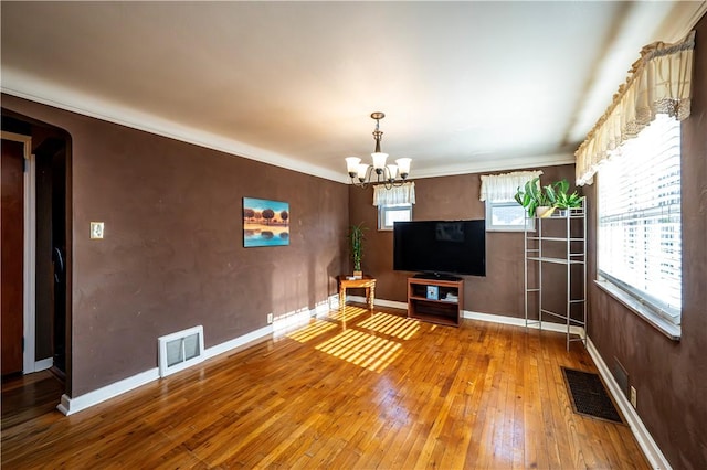 unfurnished living room with visible vents, wood-type flooring, a notable chandelier, and baseboards