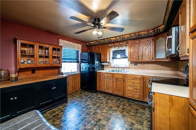 kitchen featuring glass insert cabinets, light countertops, brown cabinets, black appliances, and a sink