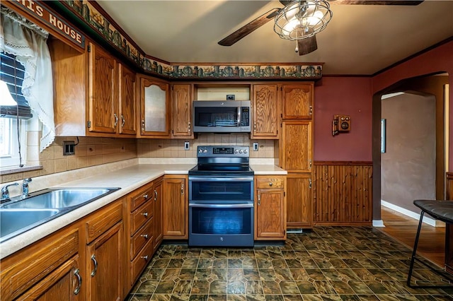 kitchen with arched walkways, appliances with stainless steel finishes, brown cabinetry, and light countertops