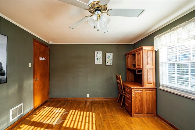 unfurnished office featuring visible vents, ceiling fan, ornamental molding, built in desk, and light wood-style flooring