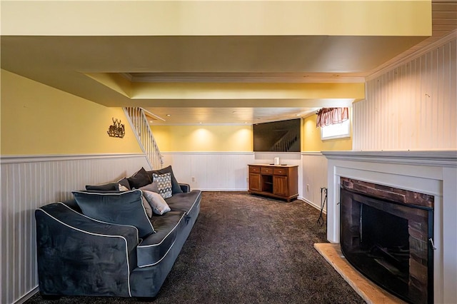 living area with a wainscoted wall, a fireplace with raised hearth, carpet flooring, and ornamental molding