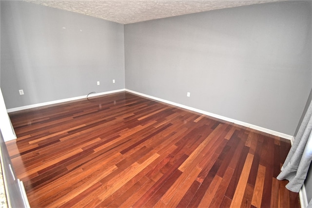 empty room with baseboards, a textured ceiling, and dark wood-style floors