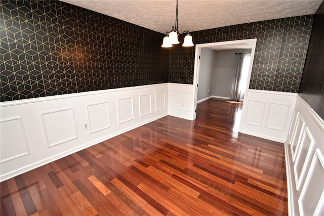 unfurnished dining area featuring dark wood-style floors, a wainscoted wall, wallpapered walls, an inviting chandelier, and a textured ceiling