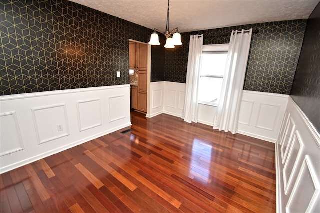 unfurnished dining area featuring dark wood finished floors, a wainscoted wall, a textured ceiling, and wallpapered walls