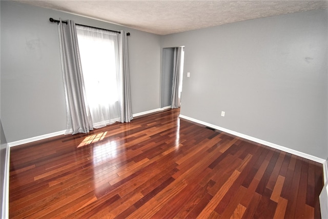 unfurnished room with visible vents, a textured ceiling, baseboards, and hardwood / wood-style floors