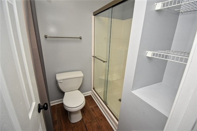 full bath featuring baseboards, toilet, wood finished floors, and a shower stall