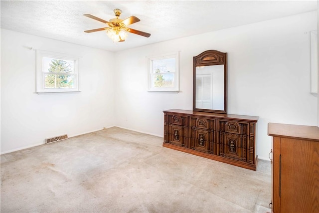 unfurnished room with visible vents, carpet floors, a textured ceiling, and a ceiling fan