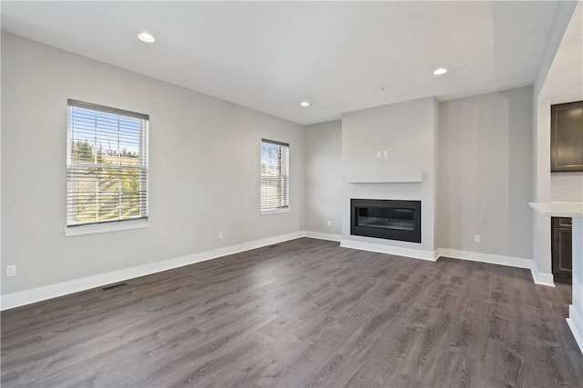 unfurnished living room featuring recessed lighting, dark wood-style floors, baseboards, and a glass covered fireplace