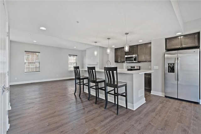 kitchen featuring an island with sink, dark wood-style flooring, dark brown cabinetry, light countertops, and appliances with stainless steel finishes