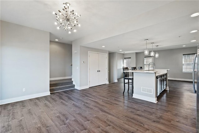 kitchen with visible vents, baseboards, light countertops, dark wood-style floors, and a kitchen island with sink