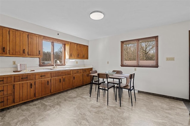 kitchen featuring brown cabinets, light countertops, baseboards, and a sink