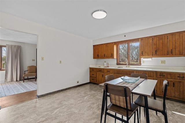 kitchen with light countertops, brown cabinetry, baseboards, and a sink