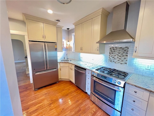 kitchen with visible vents, light wood finished floors, a sink, stainless steel appliances, and wall chimney range hood