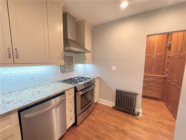 kitchen featuring radiator, stainless steel appliances, decorative backsplash, light wood-style floors, and wall chimney range hood