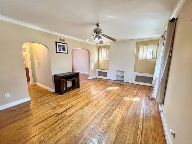 unfurnished living room featuring arched walkways, light wood-style floors, crown molding, baseboards, and ceiling fan