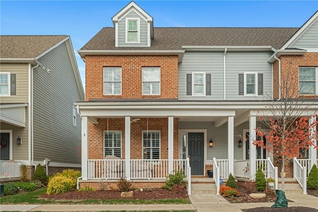 multi unit property with brick siding, covered porch, and a shingled roof