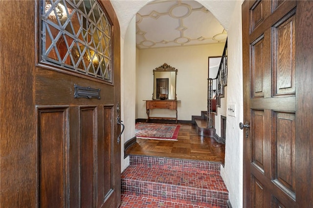 foyer entrance with brick floor, stairway, arched walkways, and baseboards