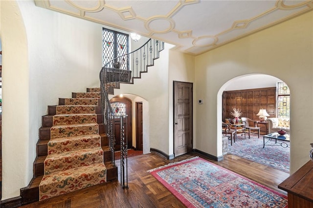 entryway featuring arched walkways, stairs, baseboards, and a towering ceiling