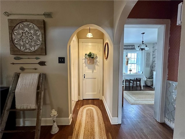 hallway featuring arched walkways, dark wood-style floors, and baseboards