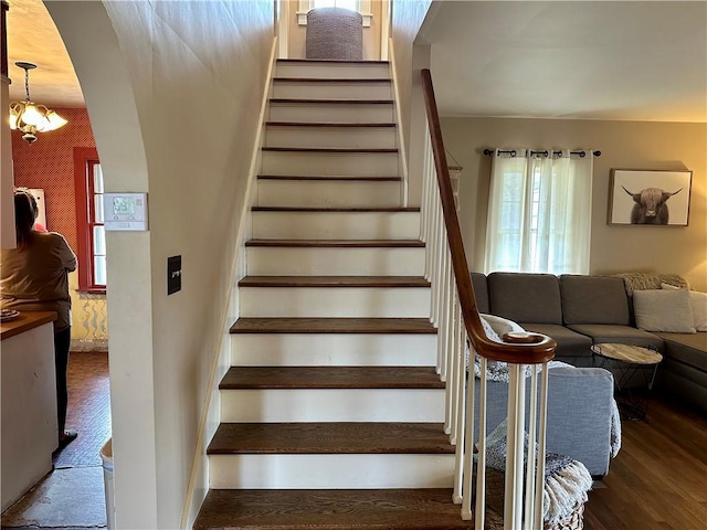 staircase with arched walkways, wood finished floors, and wallpapered walls