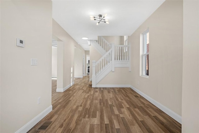 foyer entrance featuring visible vents, wood finished floors, baseboards, a chandelier, and stairs